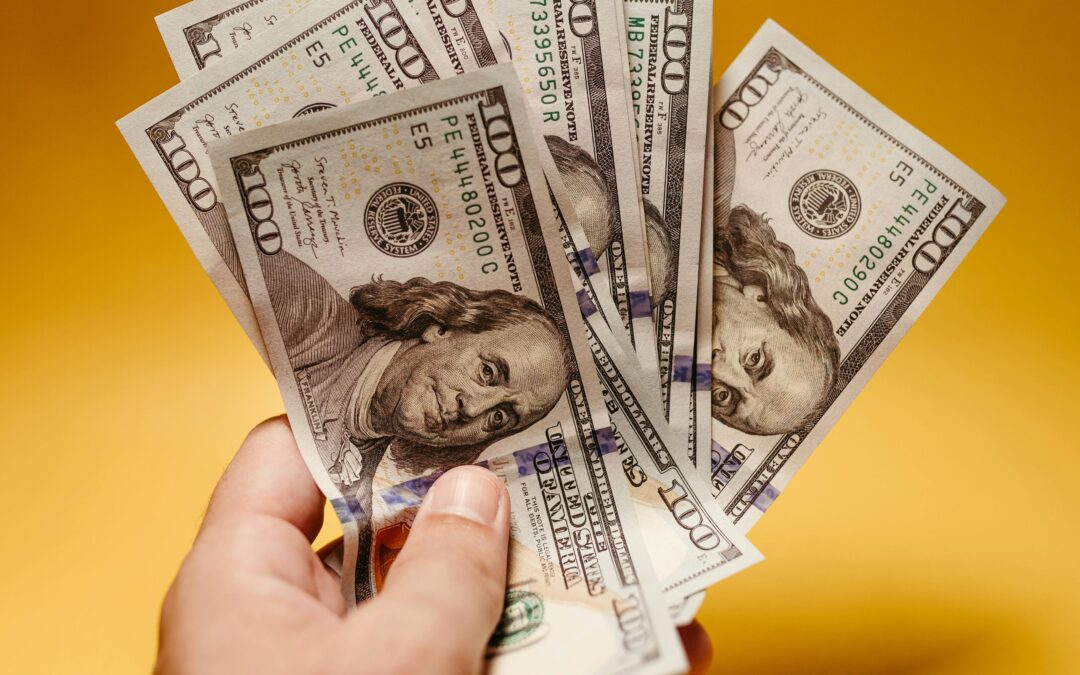 Hand holding money in front of a yellow background