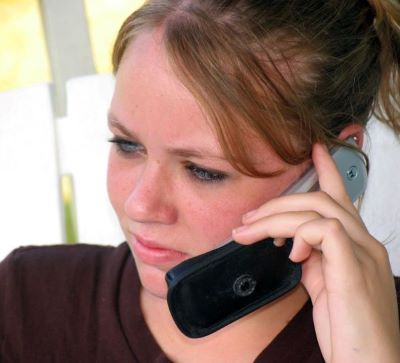 Girl with brown t-shirt looking to the left and holding phone to her ear with left hand.