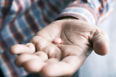 Hand of an old man with palm up holding a pink pill