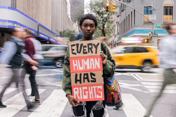 Black person standing on ped crossing with Every Human Has Rights sign