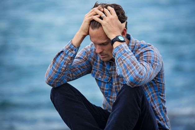 Young man with blue shirt and jeans having hands on head and looking dejected.