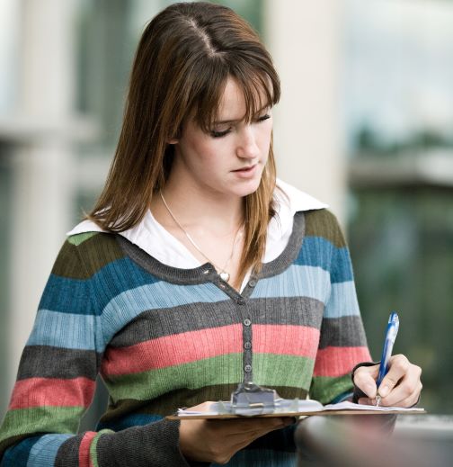 Young woman with long hair and striped sweater wrilting on a clipboard