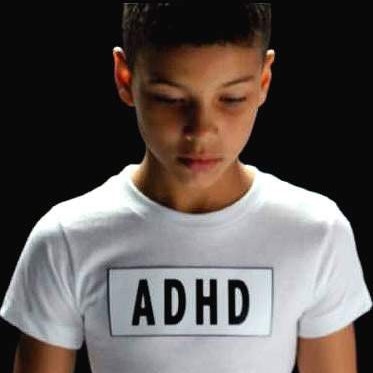 Boy with dark hair looking dejected in white t-shirt with ADHD label on front
