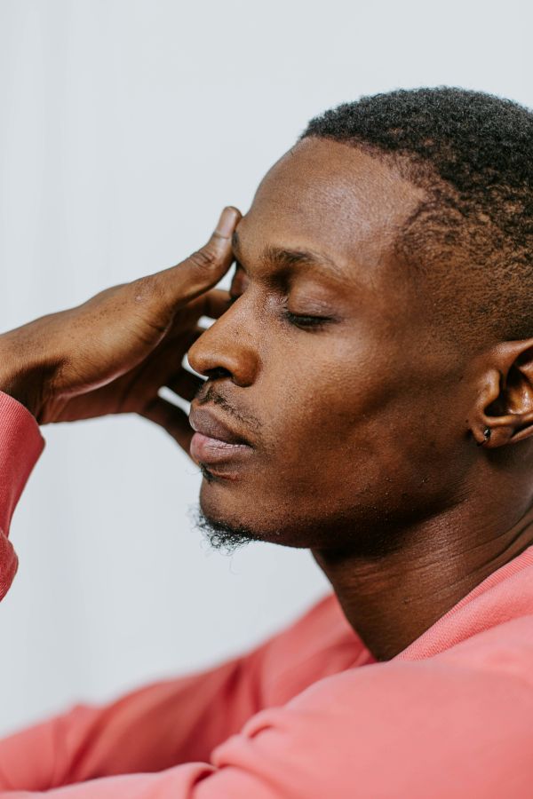 Black man with closed eyes and one hand held by forehead